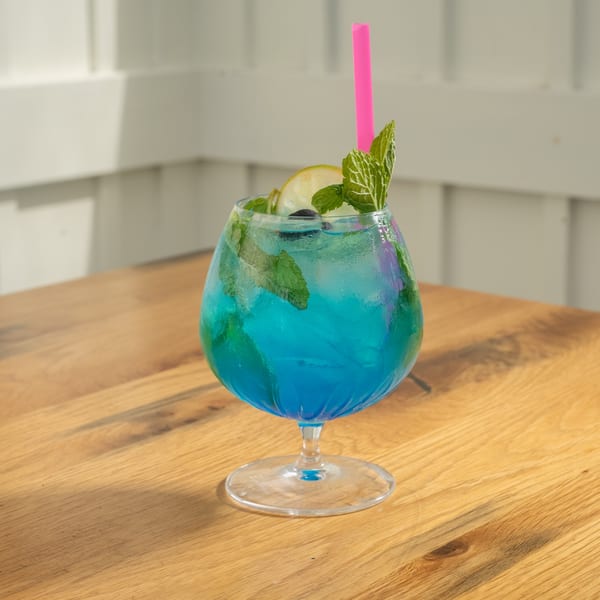 A vibrant blue cocktail with lime, mint, and a pink straw sits on a wooden table.