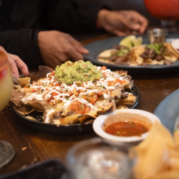 Mi Cava & Cocina's nachos with guacamole, pico de gallo, and sour cream, with hands reaching for food.
