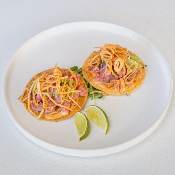 Two Mi Cava & Cocina tuna tostadas with avocado, red onion, crispy fried onions, and lime wedges.