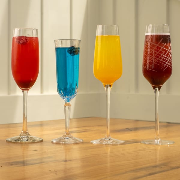 Four colorful Mi Cava & Cocina cocktails in champagne flutes on a wooden table.