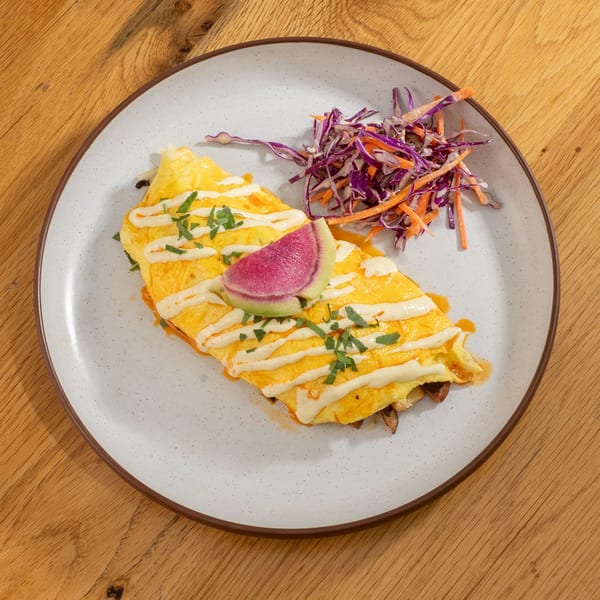 A Mi Cava & Cocina omelet with crema, herbs, and a watermelon radish slice, served with slaw.