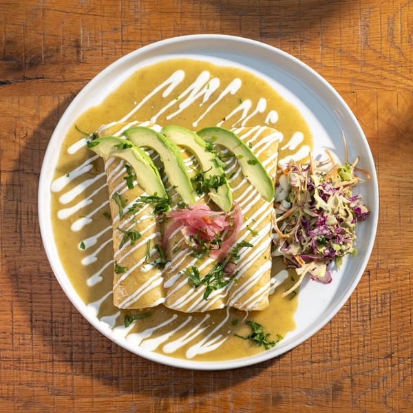 Mi Cava & Cocina's green enchiladas with avocado, pickled onions, and slaw on a white plate.