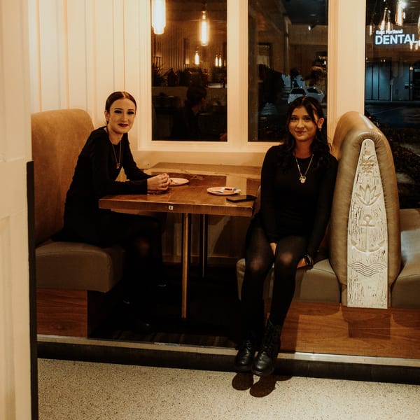 Two young women in black outfits sitting at a booth table inside Mi Cava & Cocina.