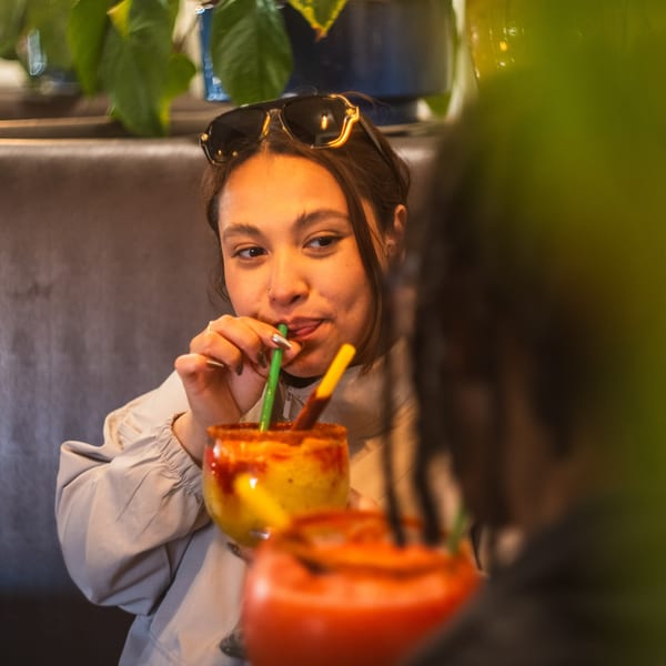 Young woman with sunglasses on her head sips a colorful Mexican drink with a green straw.