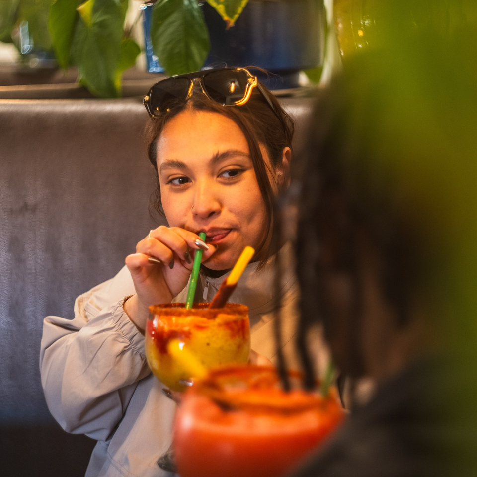 Young woman with sunglasses on her head sips a colorful Mexican drink with a green straw.