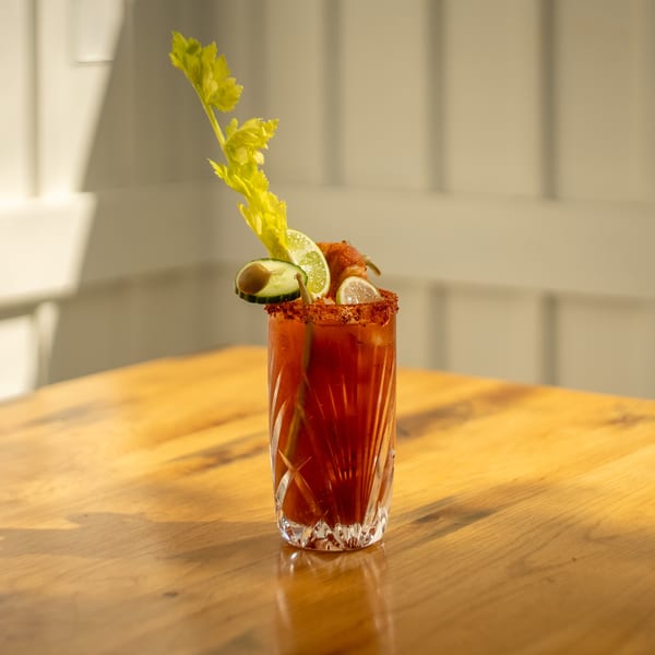 A Mi Cava & Cocina Bloody Mary cocktail, garnished with celery, lime, cucumber, and bacon.