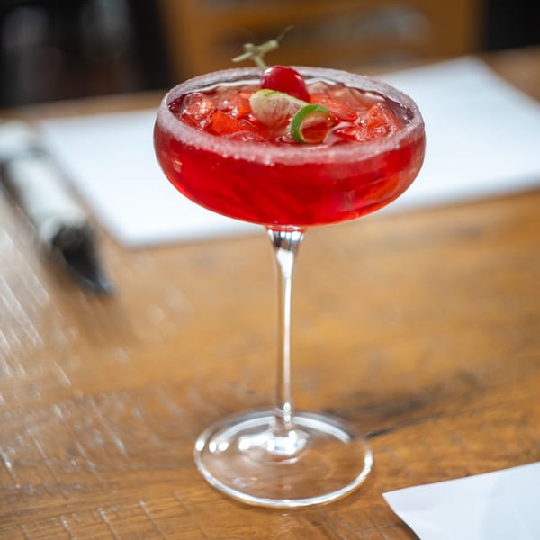 Vibrant red Mi Cava & Cocina margarita with lime and cherry garnish on a wooden table.