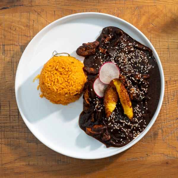 Mi Cava & Cocina's mole poblano with rice, plantains, and radish slices on a white plate.