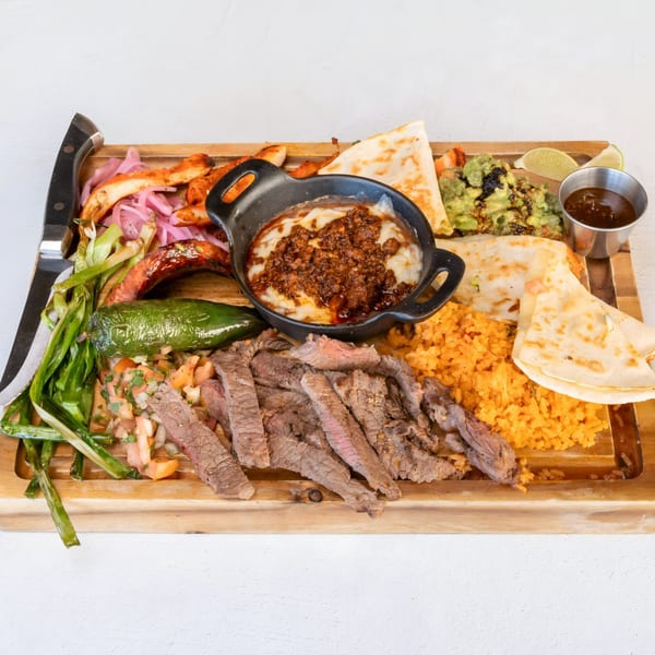 Mi Cava & Cocina's Mexican parrillada with steak, chorizo, quesadillas, rice, guacamole, and salsa on a wooden board.